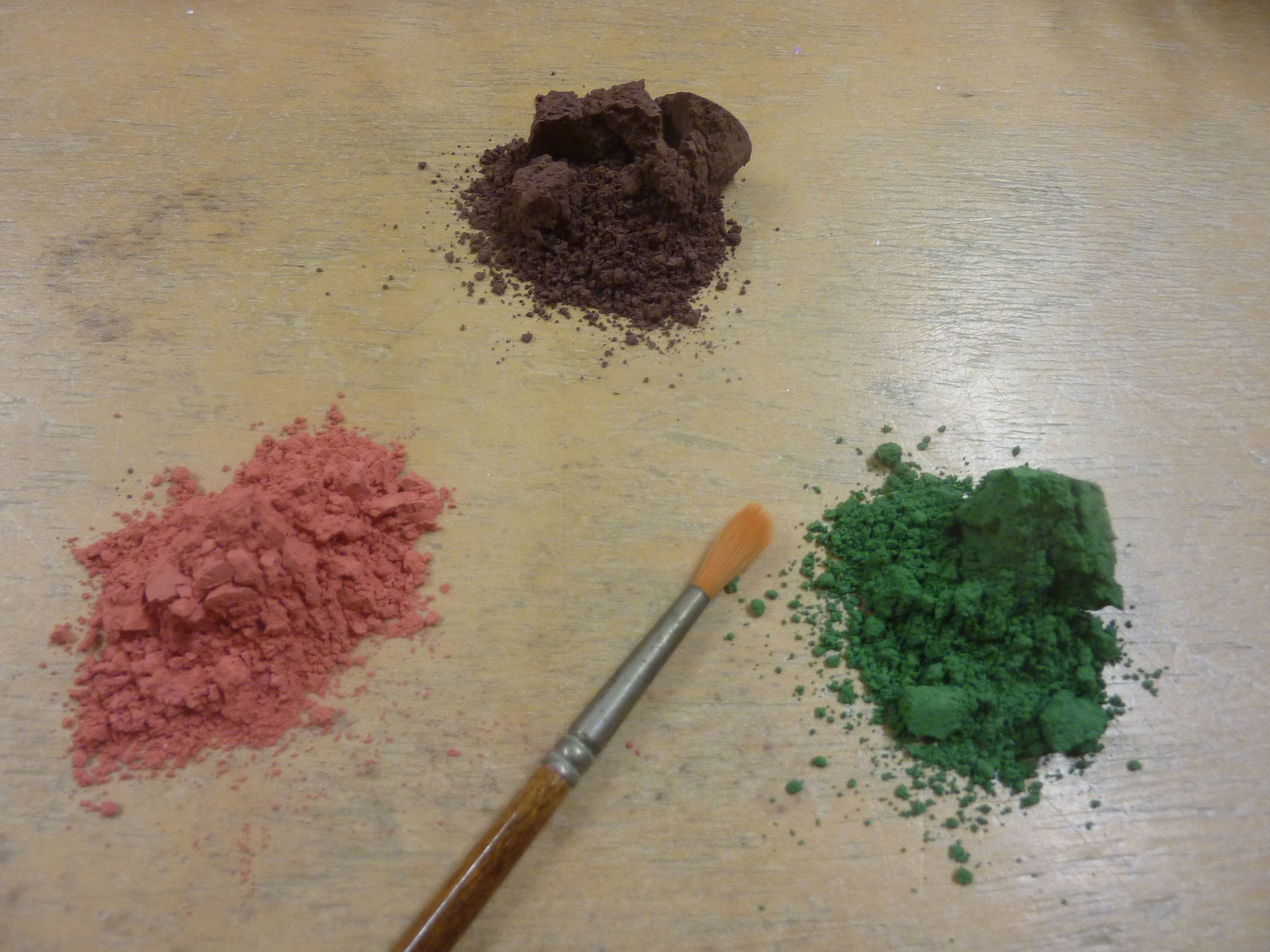 Tres montones de polvo de colores sobre una superficie de madera con un pincel.