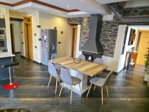 Una cocina moderna con pared de piedra, estufa empotrada y comedor con mesa y sillas de madera.