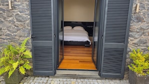 A bedroom with a bed, wooden flooring, and a stone wall.