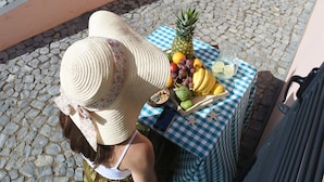 A person sitting at a table with a checkered tablecloth, a basket of fruits, and a bottle of water.