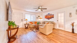 A spacious living room with hardwood flooring, a ceiling fan, and a large window with blinds. - Pool Side - Unit 114 (Mesa)