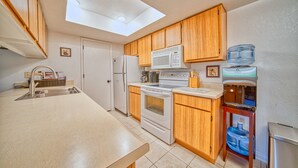 A modern kitchen with wooden cabinets, a white refrigerator, a microwave, an oven, and a water dispenser. - Pool Side - Unit 114 (Mesa)