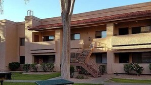 A multi-story building with a flat roof, a central staircase, and a small outdoor seating area with tables and benches. - Pool Side - Unit 114 (Mesa)