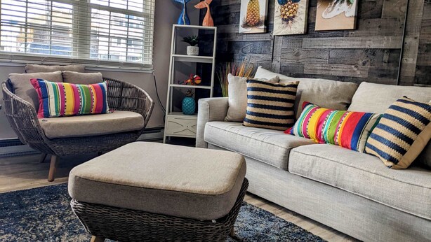 A living room with a wicker chair, a sofa, and an ottoman. There are colorful pillows on the sofa. - 1 BR Suite/1st Floor / East Side of Beach Block (Ocean City)