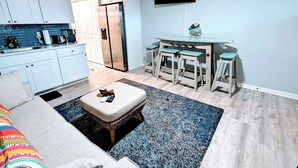 A modern kitchen with white cabinets, a built-in oven, and a refrigerator. There is a dining area with a table and four stools. A flat-screen TV is mounted on the wall above the dining area. - 1 BR Suite/1st Floor / East Side of Beach Block (Ocean City)
