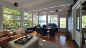 A spacious living room with large windows, a sofa, a dining table, and hanging lanterns.