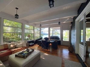 A spacious living room with large windows, a sofa, a dining table, and hanging lanterns.