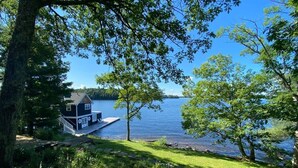 A lakeside cabin with a dock, surrounded by trees and greenery.