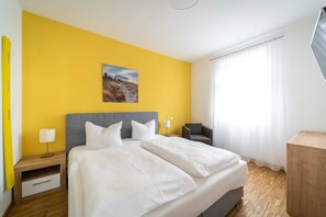 A hotel room with a large bed, a nightstand with a lamp, a chair, and a wooden side table.