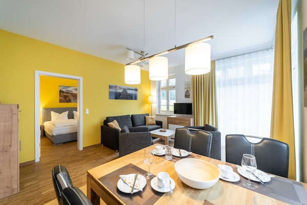 A hotel room with a dining area, a sofa, a bed, and a TV.