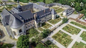 Ein Luftbild eines großen, historischen Gebäudes mit Innenhof, umgeben von Grünflächen und einem gepflegten Garten.