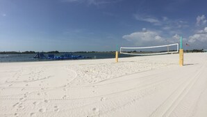 A sandy beach volleyball court with footprints, a volleyball net, and a flag.