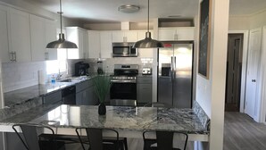 A modern kitchen with white cabinets, stainless steel appliances, a marble island with bar stools, pendant lighting, and a chalkboard wall.