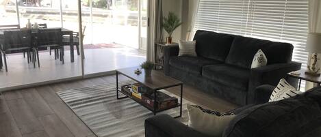 Un saló amb un sofà gris fosc, una taula de centre i una zona menjador amb cadires i una taula.