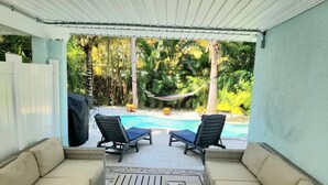 Een overdekt terras met twee lounge fauteuils en een zwembad.