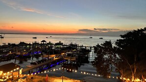 Un port de plaisance au crépuscule, avec des bateaux amarrés, une jetée parée de parasols et illuminée de guirlandes lumineuses.