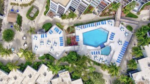 Vue aérienne d’un complexe hôtelier doté de plusieurs piscines, de chaises longues et de palmiers.