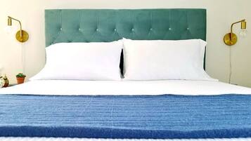 A bed with a teal upholstered headboard, white pillows, and a blue blanket. There are two wall-mounted lamps with round bases and exposed bulbs.