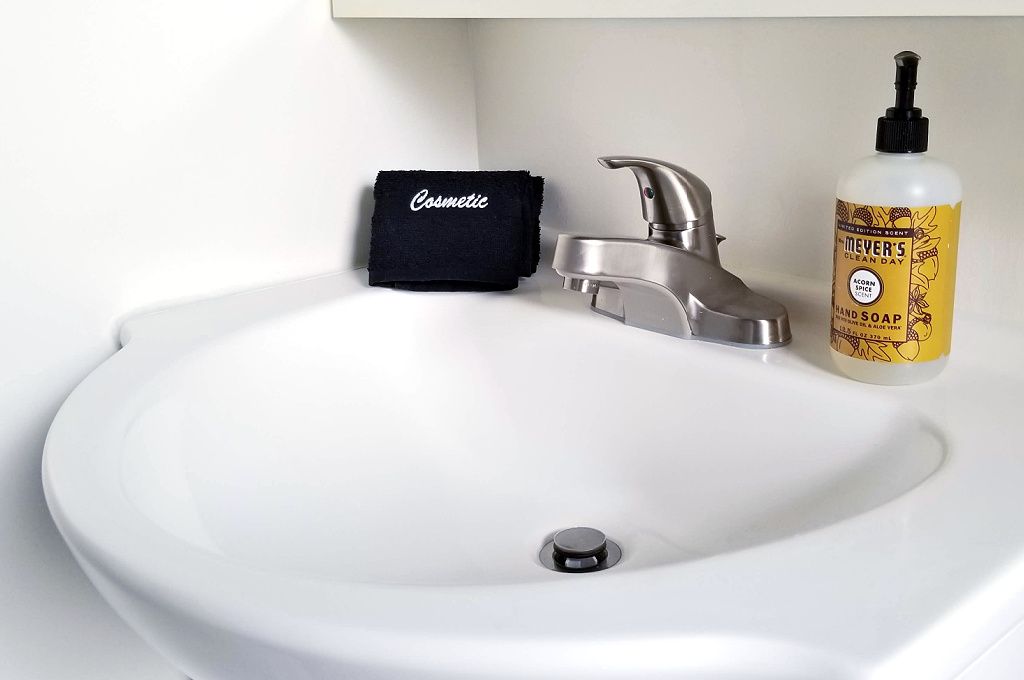 A white bathroom sink with a silver faucet, a black towel labeled "Cosmetic," and a bottle of "Meyer’s Clean Day Hand Soap."