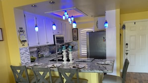 Una cocina con isla central, armarios blancos y lámparas colgantes azules.