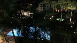 Vista nocturna de una piscina rodeada de palmeras y un edificio con ventanas iluminadas.