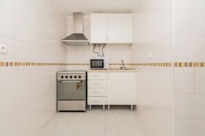 A compact kitchen with white cabinets, a stove, a microwave, and a sink. - Sun-Drenched Alfama Nest w/ Tagus River Views (Lisboa)