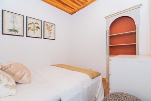 Un dormitori amb un llit, una commode i tres il·lustracions botàniques emmarcades a la paret.