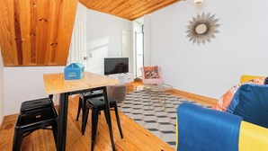 A modern living space with a wooden ceiling, a dining area with a table and chairs, a sofa, and a TV. - Sun-Drenched Alfama Nest w/ Tagus River Views (Lisboa)