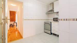 A kitchen with white tiled walls, a wooden floor, a stove, a microwave, and a cabinet with drawers. - Sun-Drenched Alfama Nest w/ Tagus River Views (Lisboa)