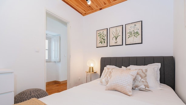 A bedroom with a bed, a bedside lamp, and three framed botanical illustrations on the wall. - Sun-Drenched Alfama Nest w/ Tagus River Views (Lisboa)