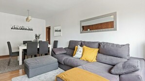 A modern living room with a grey sofa, a dining table with chairs, and a large mirror on the wall. - Bright & Spacious Three-Bed Apartment in Lisbon (Lisboa)