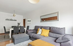 A modern living room with a grey sofa, a dining table with chairs, and a large mirror on the wall. - Bright & Spacious Three-Bed Apartment in Lisbon (Lisboa)
