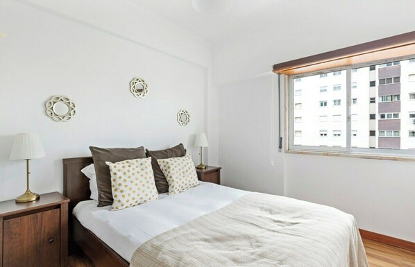 A bedroom with a bed, two bedside tables, a window, and decorative wall art.