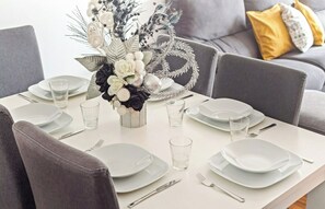 Une table à manger dressée avec de l’argenterie blanche, des verres et des couverts, agrémentée d’un arrangement floral décoratif placé au centre.