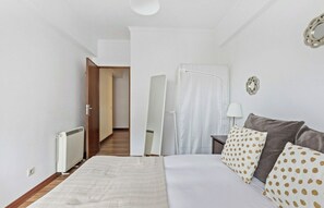 Quarto com cama, mesa de cabeceira com abajur, espelho e porta que dá para outro cômodo.