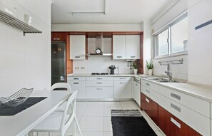 Een moderne keuken met witte kasten, een fornuis en een spoelbak. Er staat een eettafel met stoelen en een zwart vloerkleed.