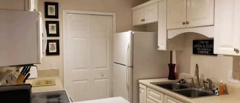 Una cocina con gabinetes blancos, un refrigerador, un lavamanos y un letrero de café.