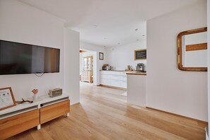 Une cuisine moderne avec des meubles blancs, un plan de travail en bois et un téléviseur à écran plat fixé au mur.