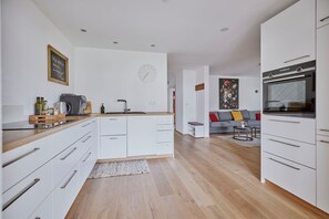 Une cuisine moderne avec des meubles blancs, un four encastré et un coin repas comprenant un canapé et une table basse.