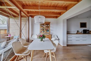 A dining area with a white table, four chairs, a hanging light fixture, and a wooden cabinet with dishes.