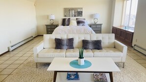 A living room with a white sofa, a coffee table, and a potted plant. There is a painting on the wall and a window with blinds. - PERFECT DESERT OASIS~lake~jet ski~boat (Truth or Consequences)