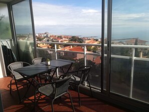 A balcony with a table and chairs, overlooking a coastal town with red-roofed buildings. - Magnifique T3 vue MER, Port de St Cyprien plage (Saint-Cyprien)