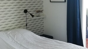 A bedroom with a bed, a hanging light fixture, a framed picture, and a window with blue curtains. - Magnifique T3 vue MER, Port de St Cyprien plage (Saint-Cyprien)