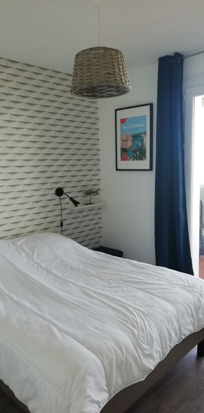 A bedroom with a bed, a hanging light fixture, a framed picture, and a window with blue curtains.