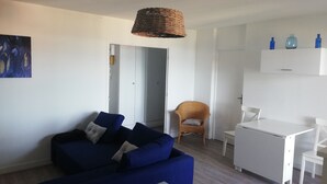 A modern living room with a blue sofa, a wicker pendant light, and a white dining area. - Magnifique T3 vue MER, Port de St Cyprien plage (Saint-Cyprien)