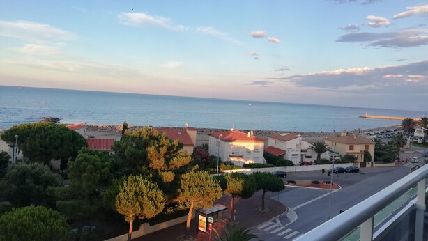 A coastal view with a clear sky, a road with a bus stop, and buildings with red roofs. - Magnifique T3 vue MER, Port de St Cyprien plage (Saint-Cyprien)
