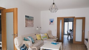 A living room with a sofa, coffee table, and a dining area in the background.