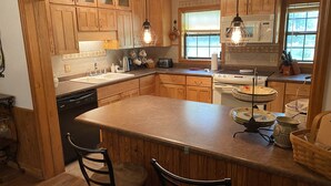 A kitchen with wooden cabinets, a central island, bar stools, a stove, and pendant lighting.