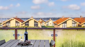 Ein Holztisch mit einer Weinflasche, einem Glas und Trauben auf einem Balkon mit Blick auf eine Reihe von gelben Häusern mit roten Dächern.