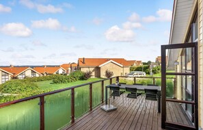 Una terraza de madera con una mesa y sillas, con vistas a una zona residencial con casas y un coche.